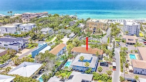 An aerial view of a coastal residential area with a prominent red flag, a swimming pool, and a beach in the background. - Gertrude's Siesta | 8-steps to Beach Path! 4-min Dining & Music! Hammocks, Snorkeling, Sunsets! (Siesta Key)