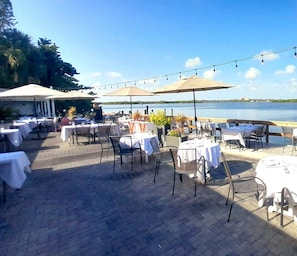 An outdoor dining area with tables and chairs, umbrellas, and a view of the water.