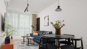 Una sala de estar moderna con un sofá, una mesa de comedor con sillas, una mesa de centro, un televisor y un jarrón decorativo con flores.