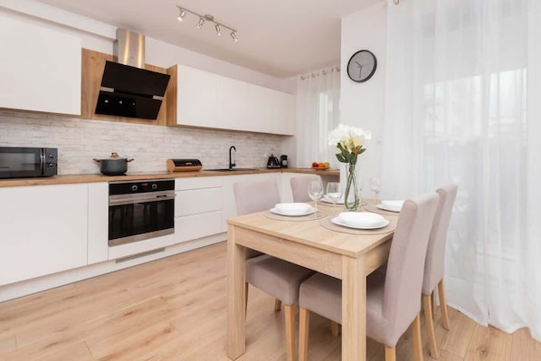 A modern kitchen with white cabinetry, a wooden countertop, and a dining area with a table set for two.
