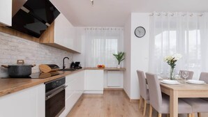 A modern kitchen with white cabinets, a wooden countertop, and a dining area with a wooden table and chairs. - Apartment with Garden | Place to Work | Close to the Lake (Gdansk)