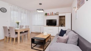 A modern living room with a dining area, a sofa, a coffee table, a TV, and a kitchen area. - Apartment with Garden | Place to Work | Close to the Lake (Gdansk)