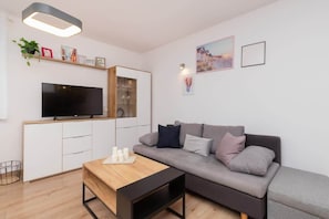 A modern living room with a grey sofa, a wooden coffee table, a flat-screen TV, and a built-in cabinet with glass doors.