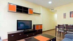 Un soggiorno con televisore a schermo piatto, mobile TV in legno scuro, pannelli decorativi arancioni, un divano e un'area pranzo con sedie.