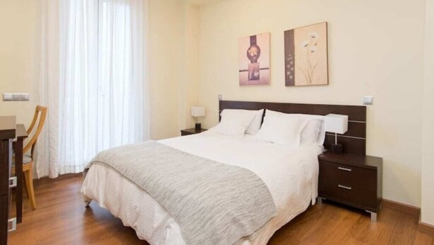 Una camera da letto ordinata con un letto grande, un comodino, una sedia e due quadri appesi al muro.