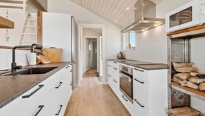 Moderni keittiö, jossa on valkoiset kaapit, puinen työtaso ja sisäänrakennettu uuni.