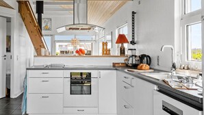 Cocina moderna con muebles blancos, horno empotrado, cafetera y ventana con vistas a zonas verdes.