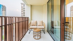 Un balcón con una silla de mimbre y cojines, un ventanal de vidrio y vistas a un edificio en construcción.