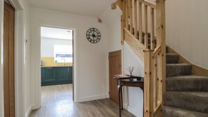 Una escalera con barandillas de madera que lleva a una plataforma, una zona de cocina con armarios verde azulado y un reloj de pared.