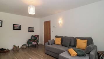 A living room with a grey sofa, a wooden floor, a green armchair, and a white door.