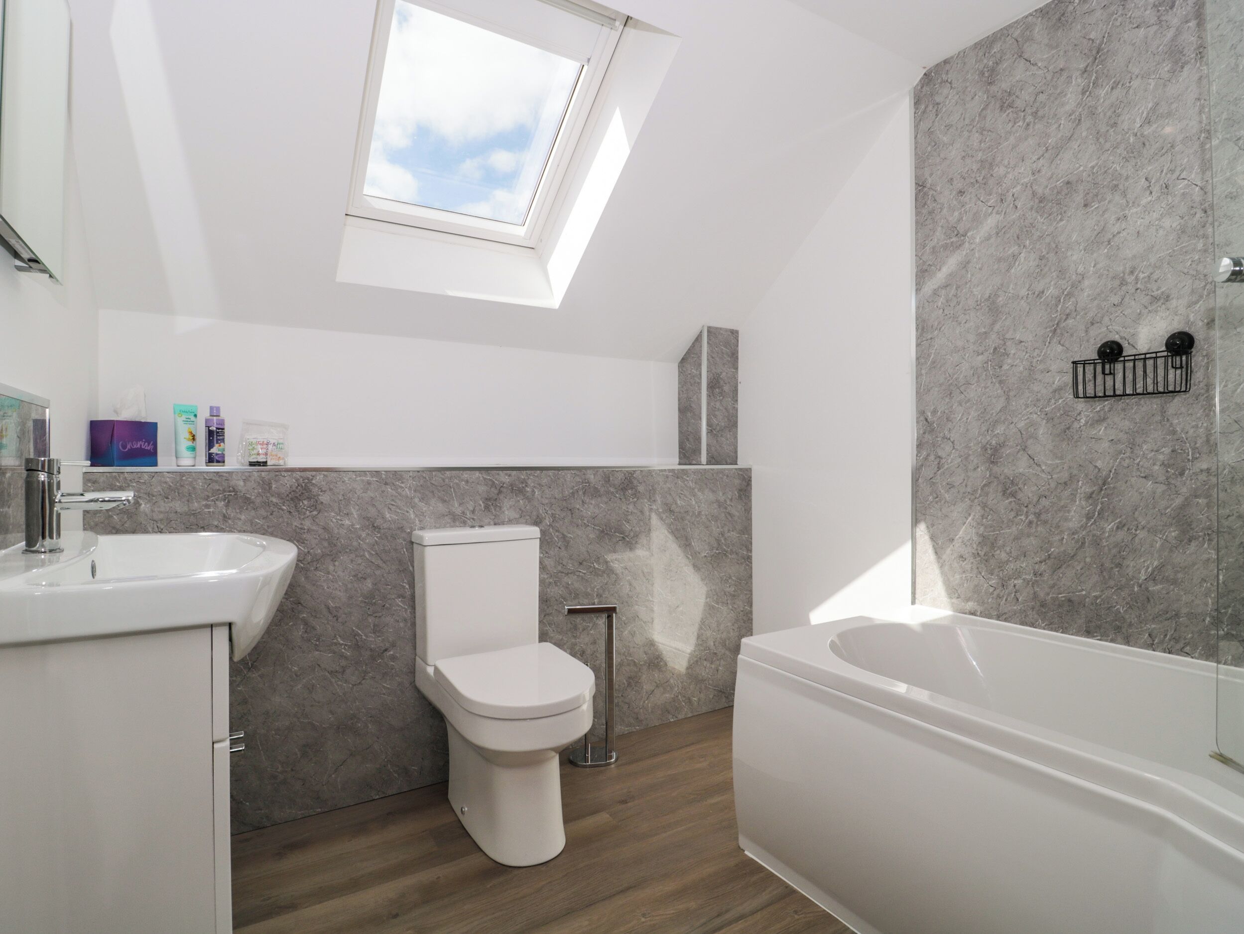 A modern bathroom with a skylight, a toilet, a sink, and a bathtub.