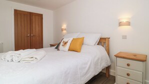 Una cama bien hecha con edredón blanco, una mesita de noche de madera con cajones y un armario de madera.