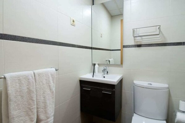 Une salle de bain avec des carreaux blancs, un meuble noir, un lavabo blanc et des toilettes.