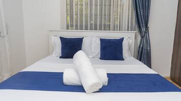 Een net opgemaakt bed met wit en blauw beddengoed, twee kussens en opgerolde handdoeken.