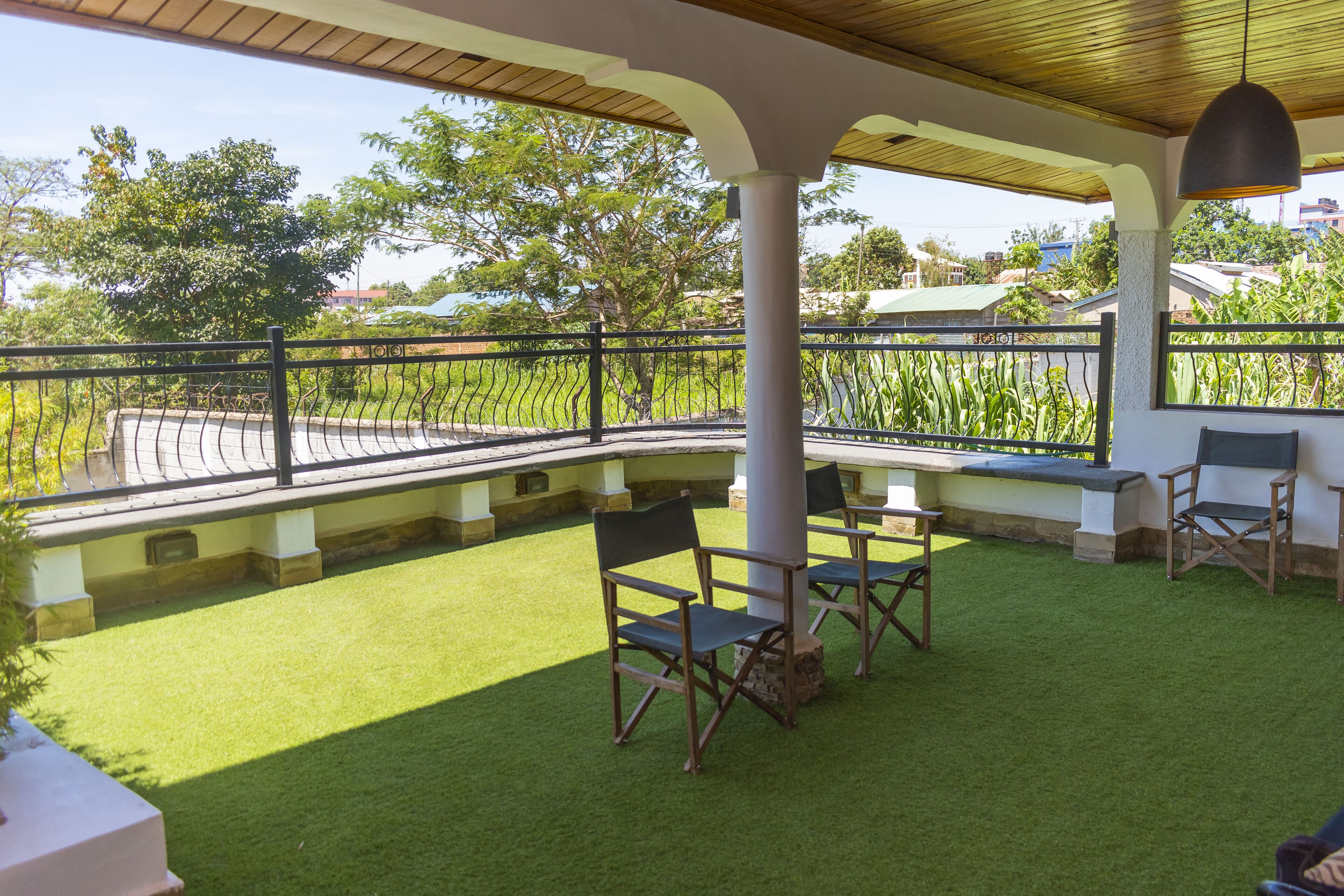 Un patio exterior con césped artificial, una pérgola de madera y vistas a un jardín y edificios al fondo.