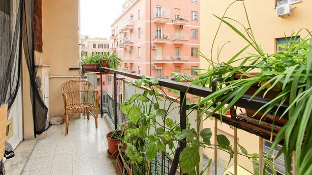 A balcony with a wicker chair, potted plants, and a view of adjacent buildings. - Large & Quiet Home in Rome Monteverde (Roma)