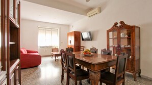 A dining area with a wooden table, chairs, and a fruit bowl. There is a red sofa and a television on the wall. - Large & Quiet Home in Rome Monteverde (Roma)