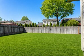 A backyard with a wooden fence, a well-maintained lawn, and houses in the background. - Two Adjacent Apartments for Large Groups (3539) (Boise)