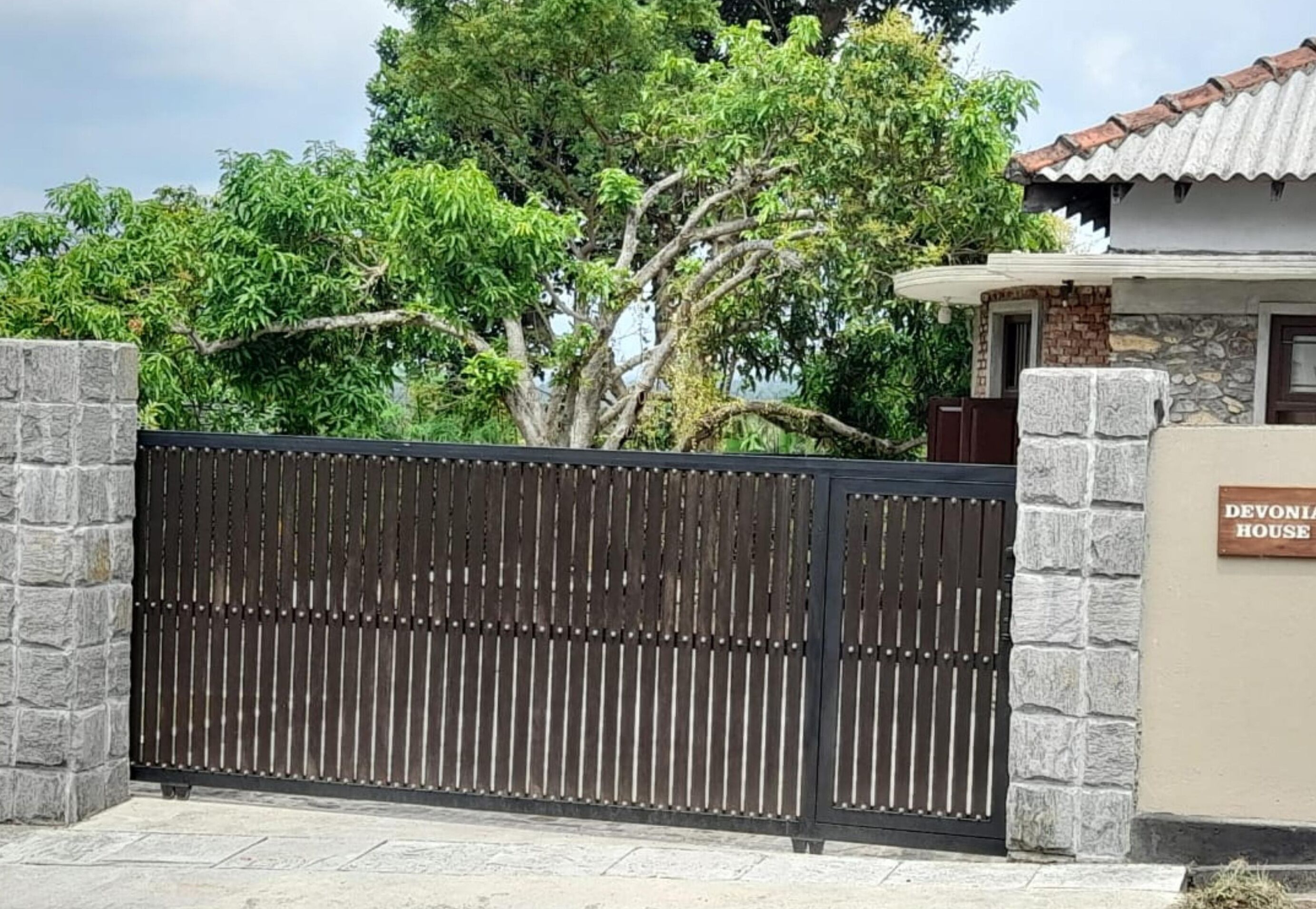 A gated entrance with a stone wall and a sign reading "DEVON HOUSE".