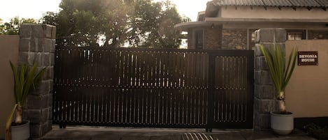 A gated entrance to a property named 'Devonia House' with a stone wall and potted plants.