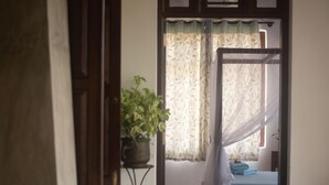 Een kamer met een bed, een kamerplant en een raam met gordijnen.
