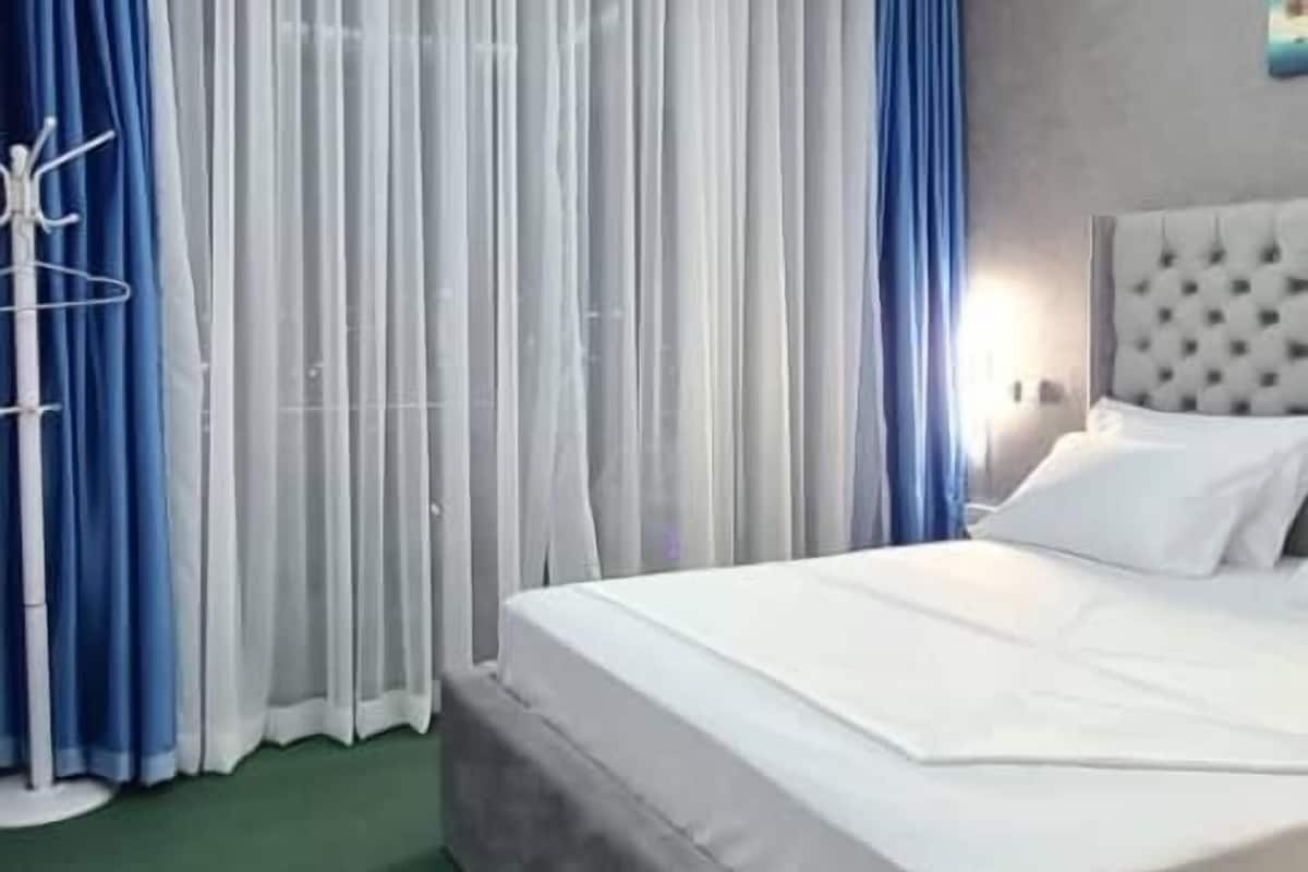 Une chambre d’hôtel moderne avec un grand lit, une moquette verte et un luminaire au plafond.