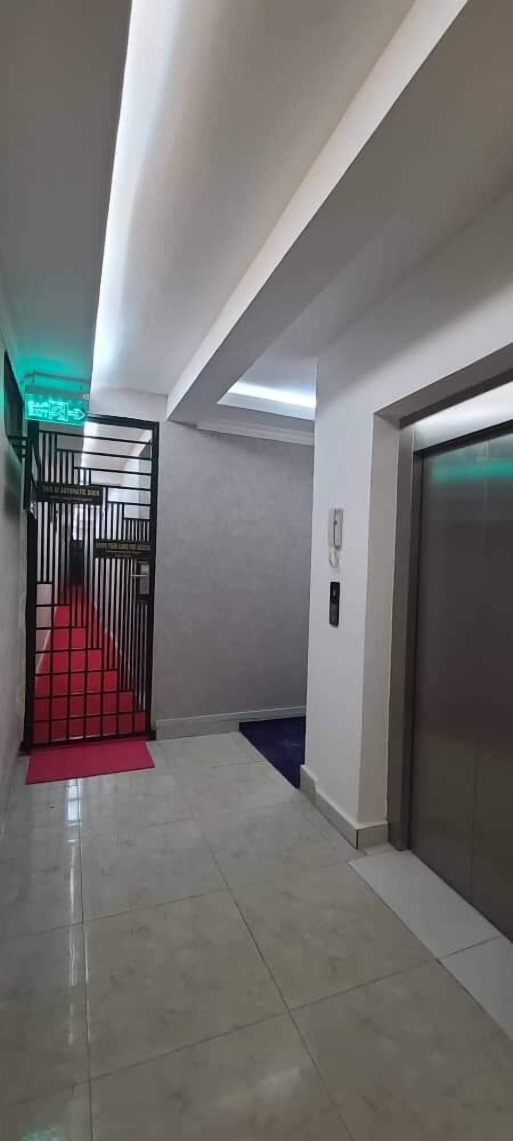 Un pasillo con alfombra roja que conduce a una puerta, un ascensor blanco y suelo de baldosas.