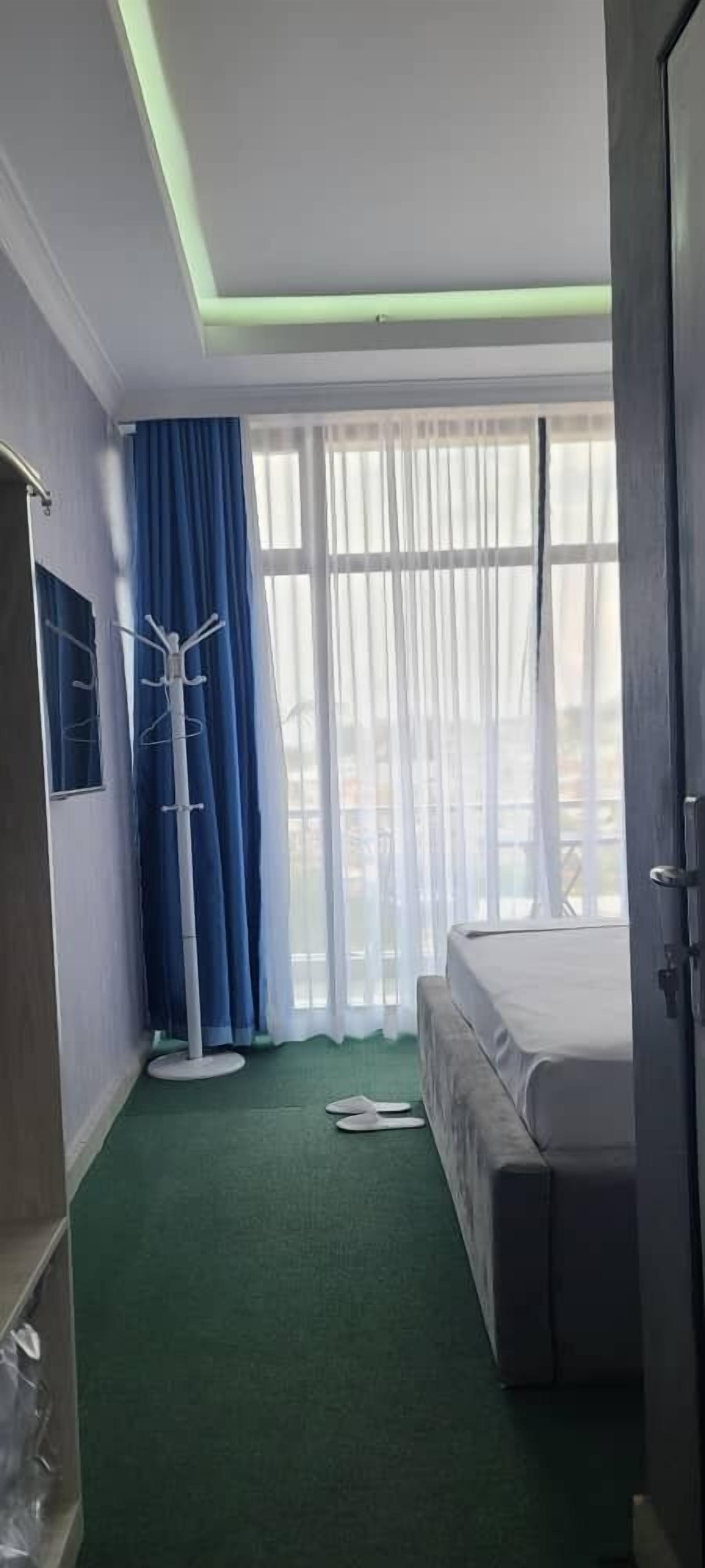 A hotel room with a bed, a coat rack, a floor lamp, and a window with curtains.