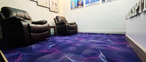 A room with two leather recliners, a patterned carpet, and a wall with framed pictures.