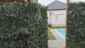 A stone pathway leading to a wooden pergola in a garden area with a pool in the background. - Private Pool, Hot Tub, Luxury Cabana Poole Dorset. (Poole)