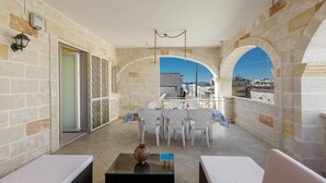 A balcony with stone walls, a dining area with white chairs and a table, and a view of the city. - 3777 Appartamento Space Family by Barbarhouse (Manduria)