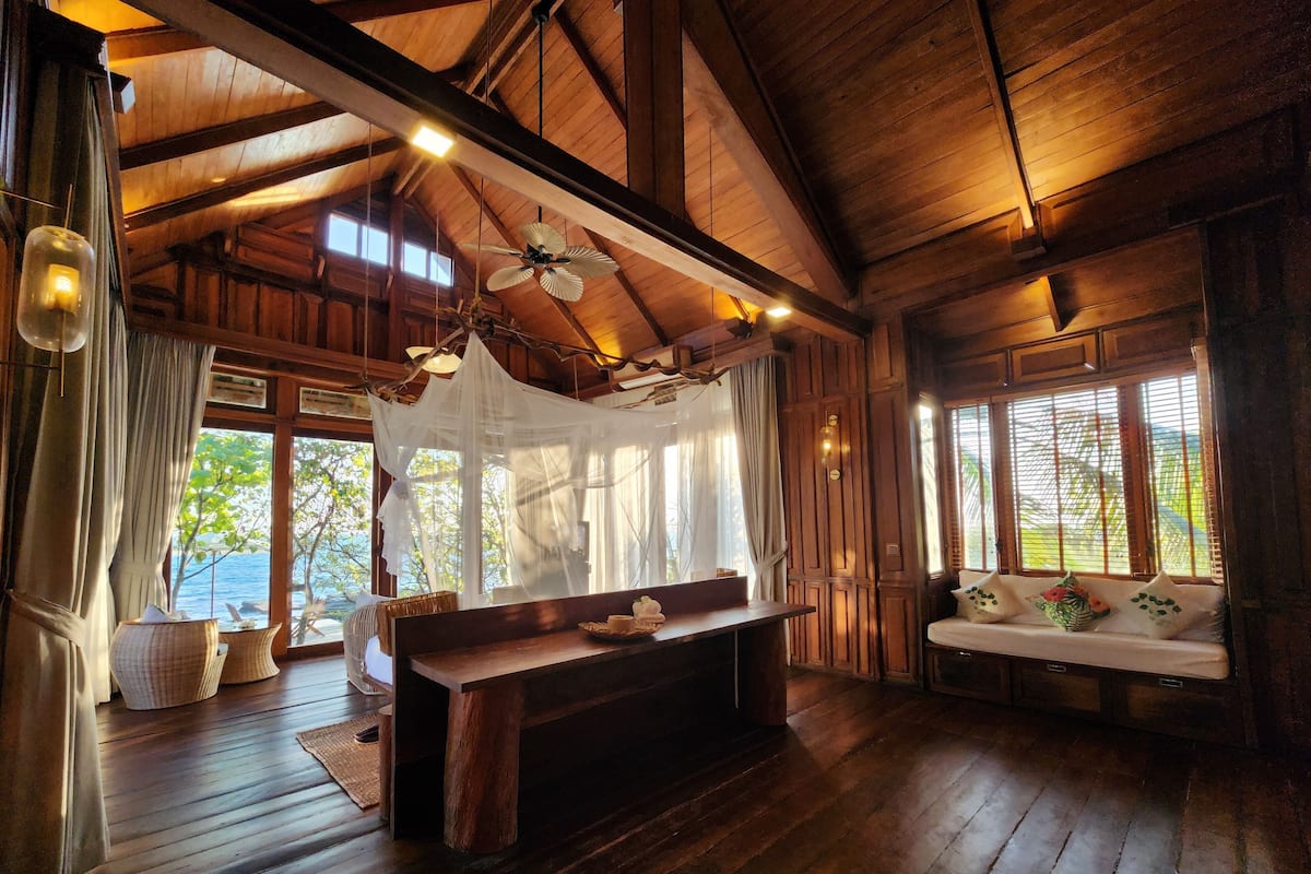 A wooden interior with a large wooden bench, a ceiling fan, and a view of the outdoors through large windows.