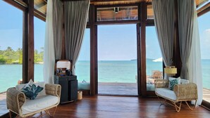 A room with wooden flooring, two wicker sofas with cushions, a small table, and a view of the ocean through large windows. - Full Moon Private Island (Kiri Sakor)
