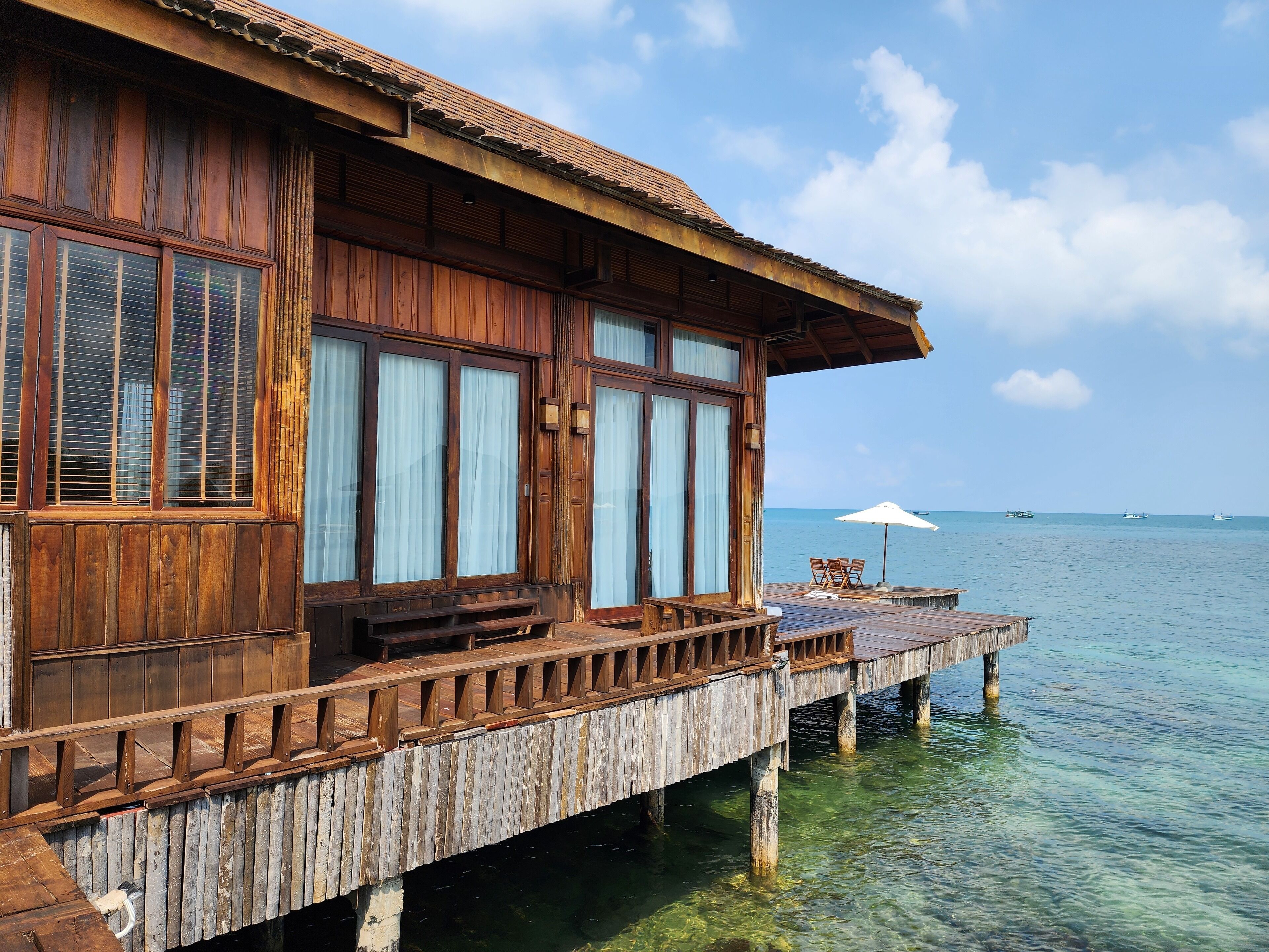 A wooden overwater bungalow with large windows, a wooden deck, and a clear view of the ocean.