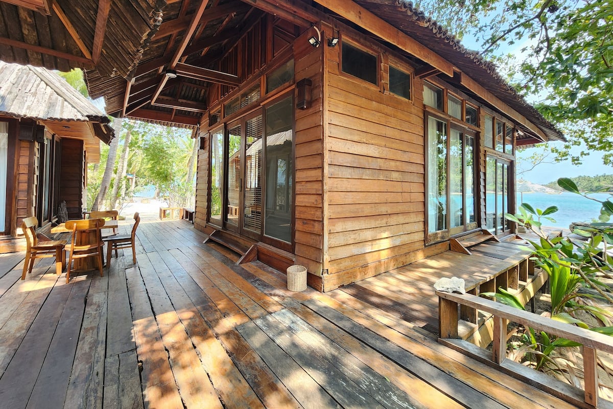 A wooden cabin with a porch, large windows, and a view of the water.