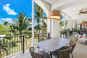 Un balcon spacieux avec un coin repas, de grandes fenêtres et une vue sur les palmiers.