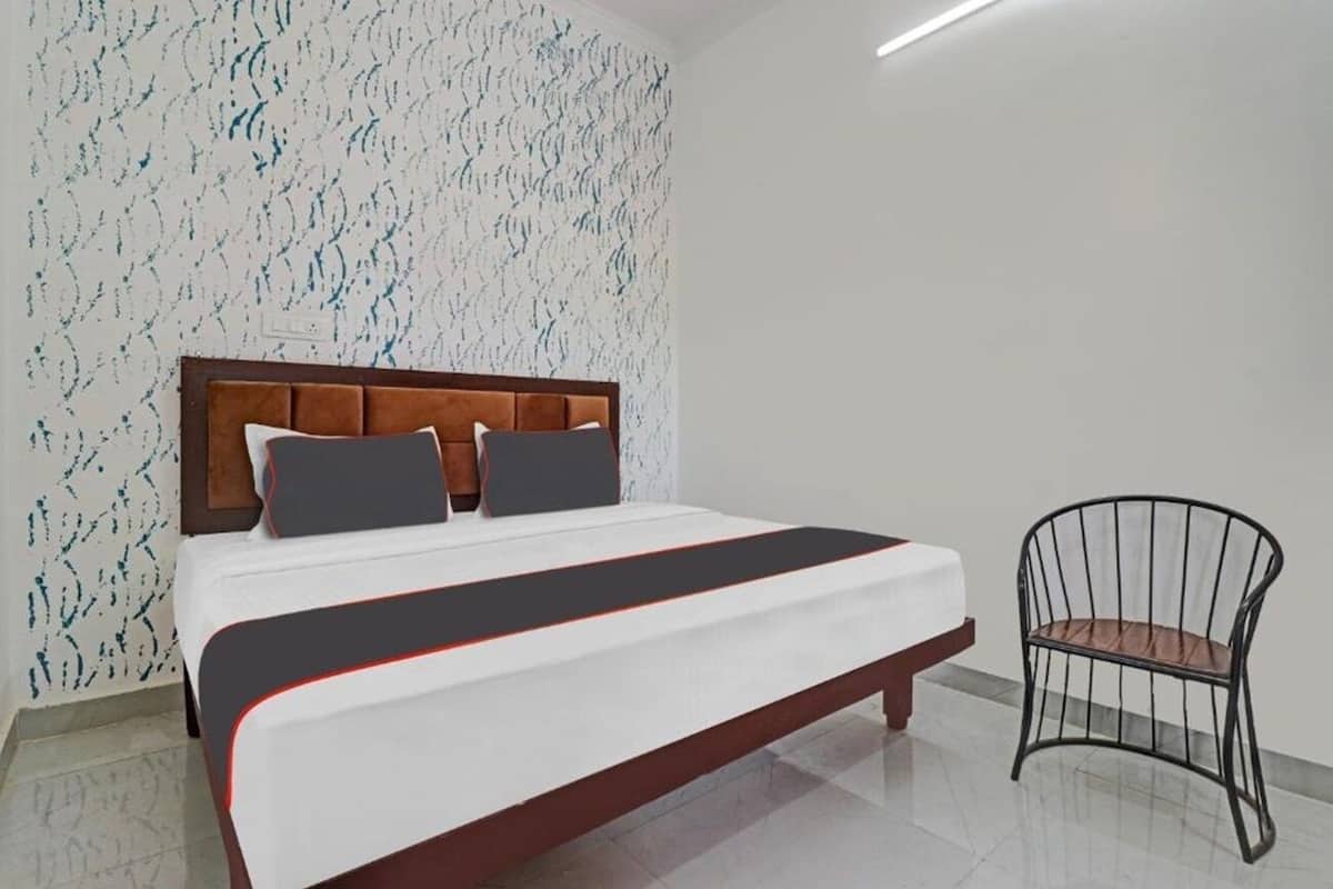 Una cama bien hecha con cabecera de madera, una silla de metal y un papel tapiz estampado.
