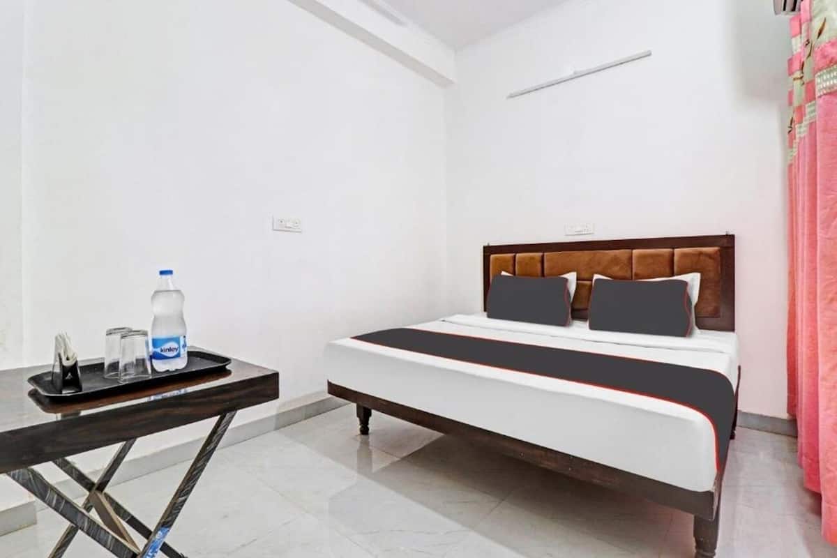 Una habitación de hotel con una cama, una mesita con una bandeja que contiene una botella y vasos, y una cortina.