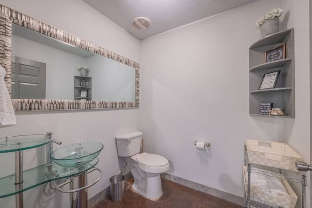 A bathroom with a glass sink, a toilet, and a shelf with decorative items.