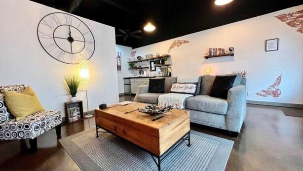 Ein modernes Wohnzimmer mit Couchtisch aus Holz, zwei Sofas, einer Wanduhr und einer Küche im Hintergrund.