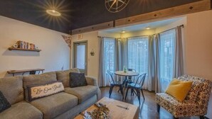 Ein gemütliches Wohnzimmer mit einer Couch, einem gemusterten Sessel, einem Couchtisch und einem Essbereich mit Tisch und Stühlen.