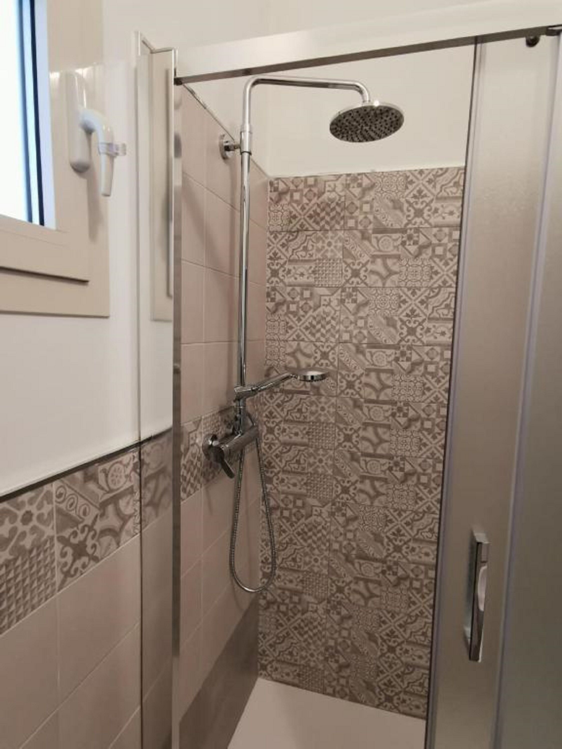 A shower with a handheld showerhead and a wall-mounted showerhead, tiled with patterned tiles.
