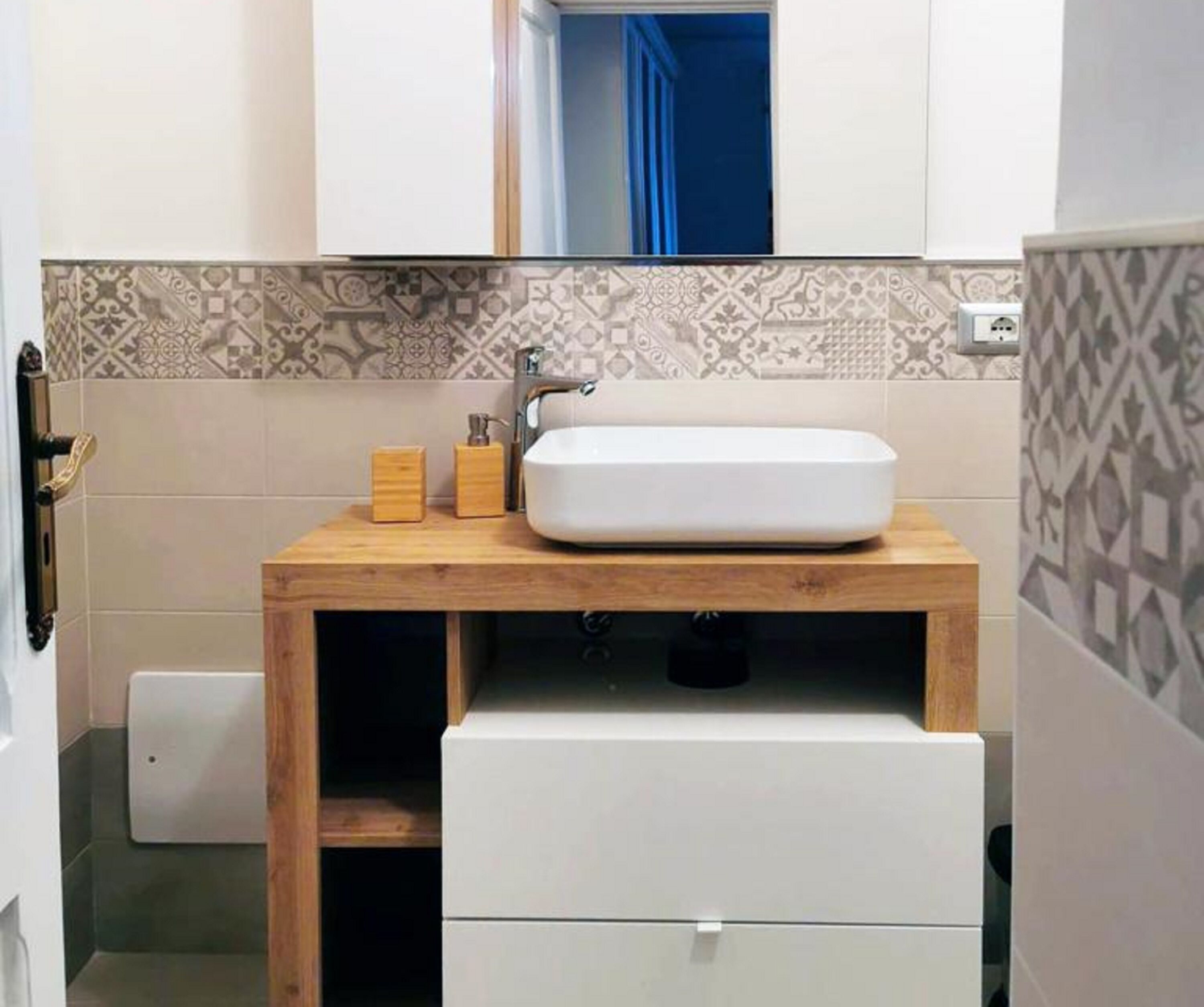 A bathroom with a white sink, wooden countertop, patterned tiles, and a small wooden cabinet.