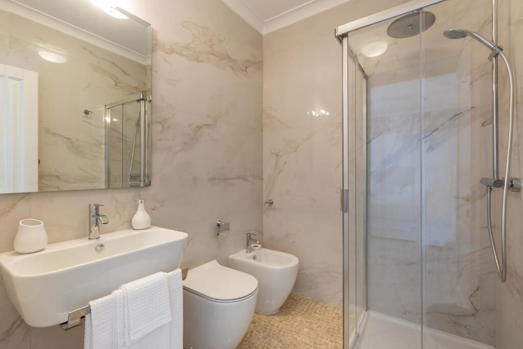 A modern bathroom with a glass-enclosed shower, a pedestal sink, and a bidet.