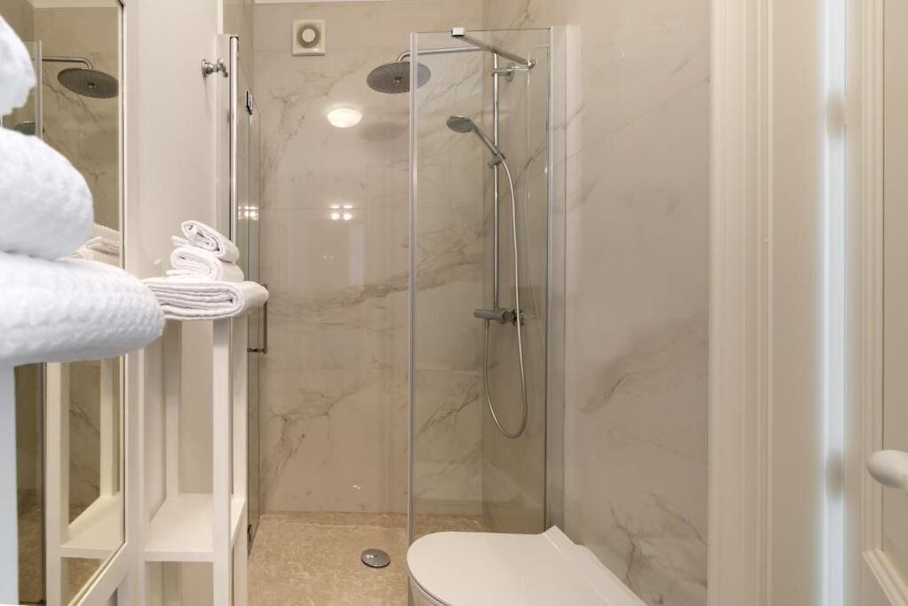 Un baño moderno con ducha envuelta en vidrio, un inodoro blanco y toallas ordenadas en una estantería.