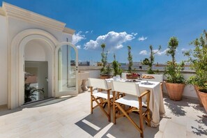 A rooftop terrace with a table set for dining, potted plants, and a clear view of the city skyline. - Relais Carlo Alberto (Salve)