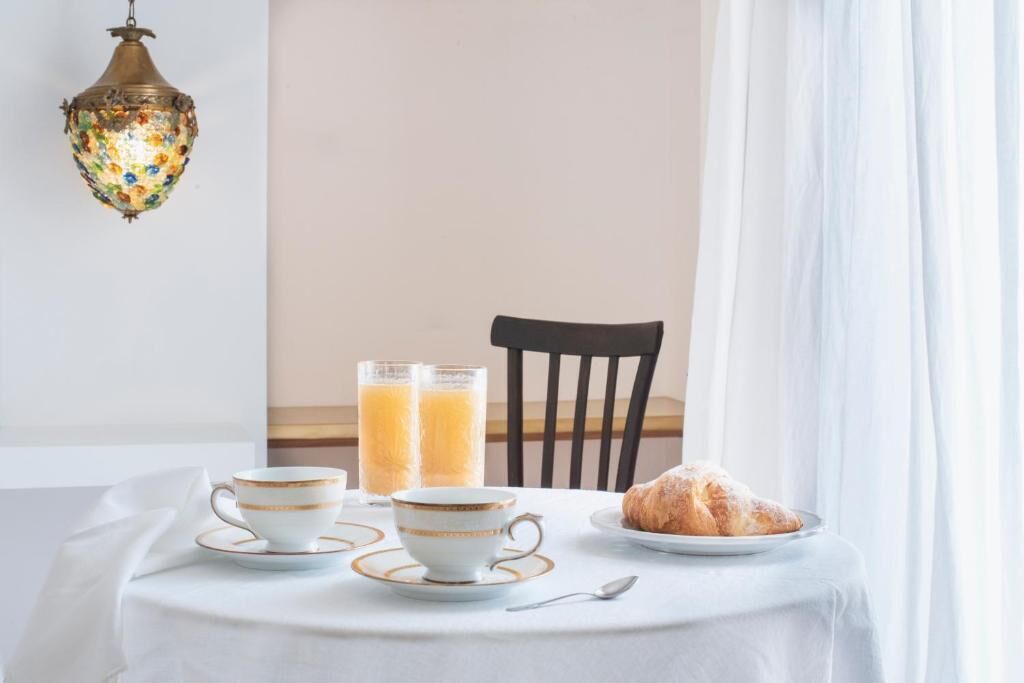 A breakfast setup with two cups, two glasses of orange juice, a croissant, and a spoon on a table.