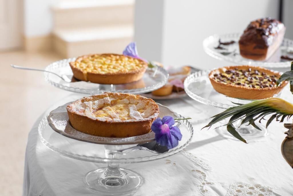 Una mesa con tres fuentes de vidrio para tarta sobre un mantel blanco.