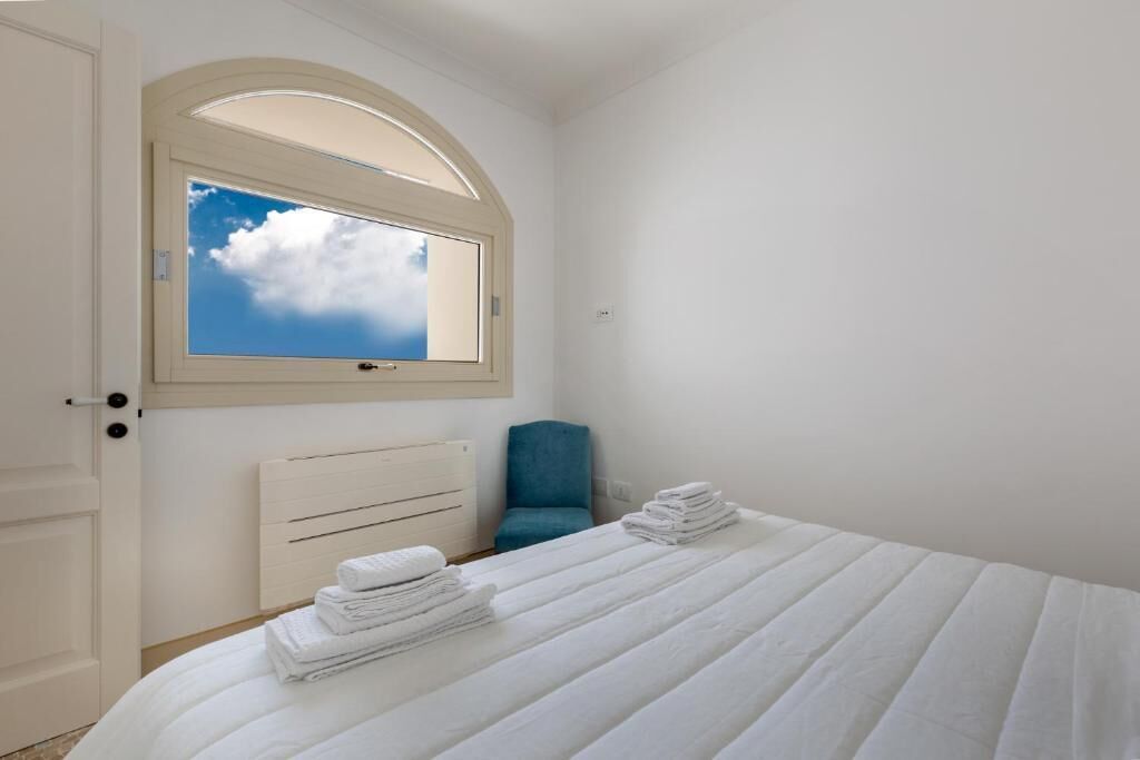 Een slaapkamer met een bed, een raam met uitzicht op de lucht, een stoel en een radiator.
