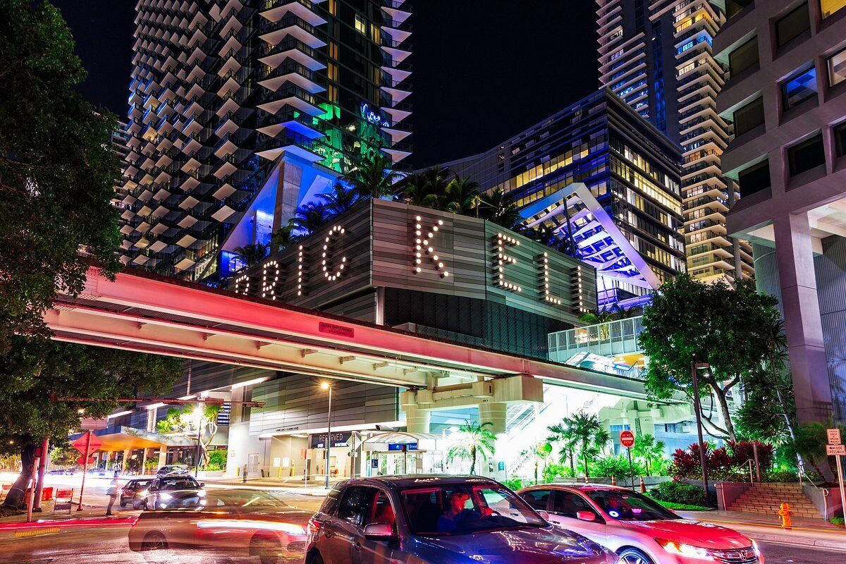 A modern hotel with a prominent 'HOTEL' sign, a covered walkway, and high-rise buildings in the background.